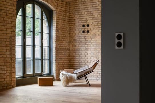 Saniertes Loft in einem Altbau mit mattschwarzen Balken und einer offenen Backsteinwand und schwarzen Loft-Kastenfenstern.