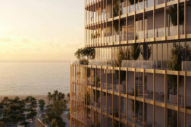 Modern high-rise building with glass balconies featuring potted plants, overlooking a beach and ocean at sunset.