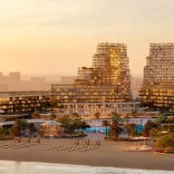 Sunset view of a beachfront resort with modern high-rise buildings, lush greenery, and rows of lounge chairs on the sandy shore.