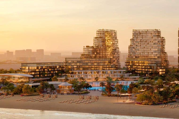 Sunset view of a beachfront resort with modern high-rise buildings, lush greenery, and rows of lounge chairs on the sandy shore.