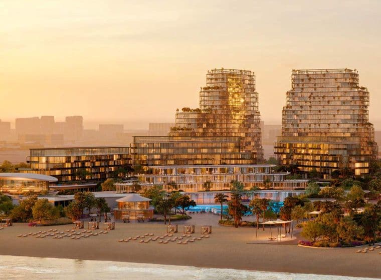 Sunset view of a beachfront resort with modern high-rise buildings, lush greenery, and rows of lounge chairs on the sandy shore.