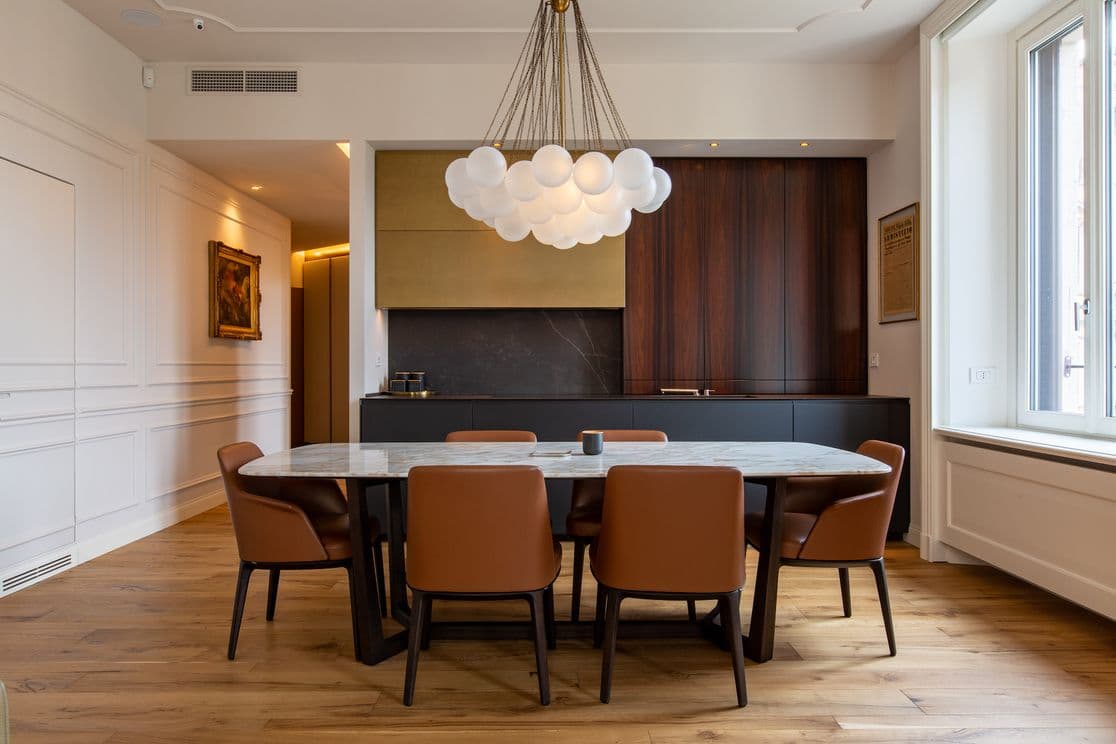 Modernes Esszimmer mit Marmortisch, braunen Lederstühlen, einem wolkenartigen Kronleuchter und Holzboden. Großes Fenster auf der rechten Seite.