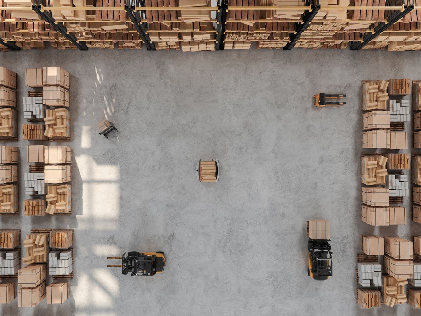 Aerial view of a warehouse with stacked boxes, two forklifts, and shelves filled with packages, on a concrete floor.