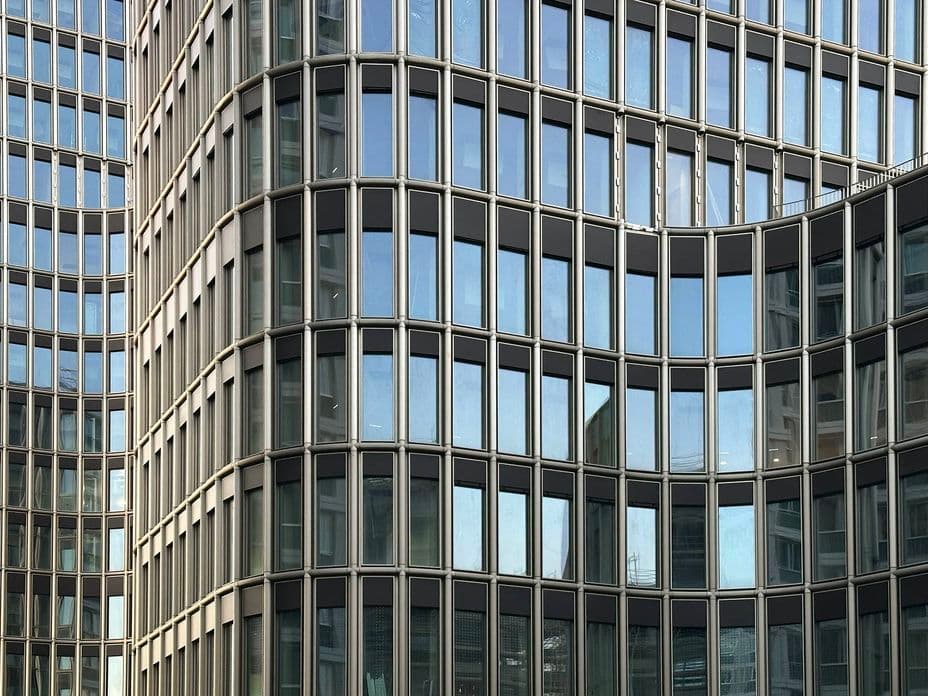 Tall modern office building with a grid of reflective glass windows, creating a sleek and symmetrical façade against a blue sky.
