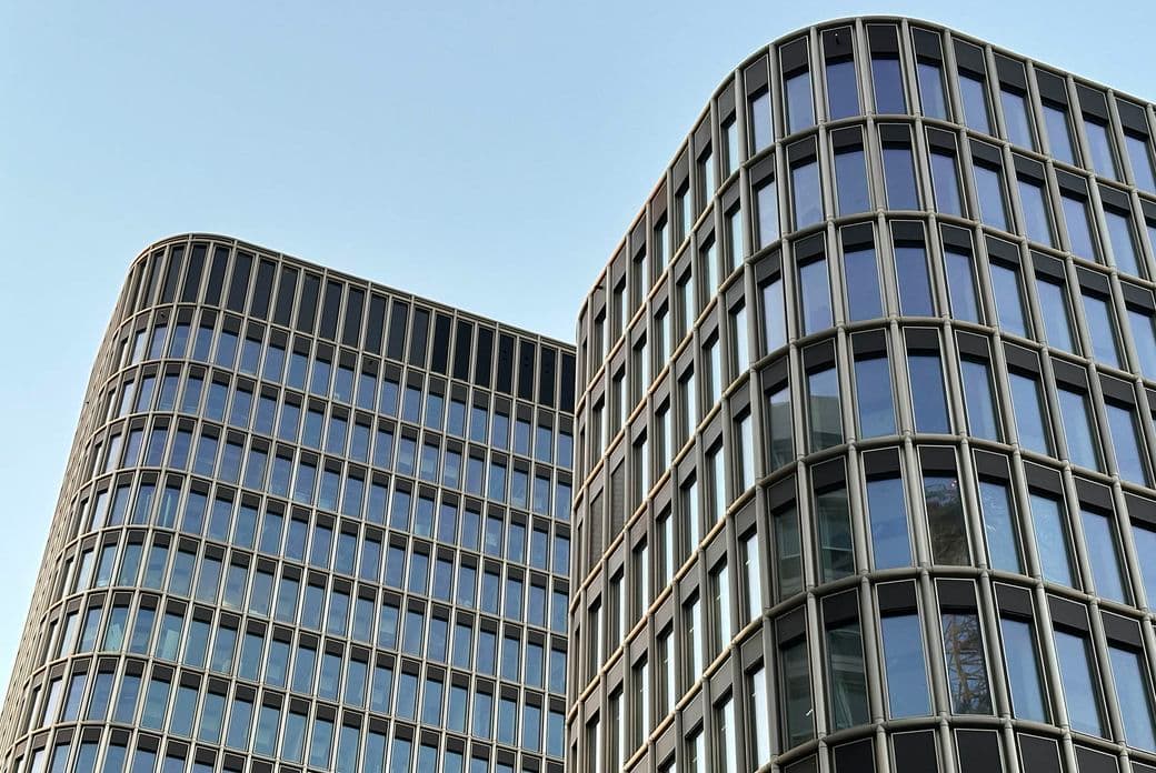 Zwei moderne Gebäude mit geschwungenen Fassaden und reflektierenden Glasfenstern vor einem klaren blauen Himmel.
