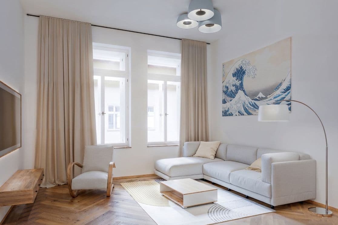 Living room with herringbone wooden flooring. A light-colored sectional sofa stands against the wall with a coffee table on a pale area rug, accompanied by an arched floor lamp. Opposite is a TV wall with a low wooden cabinet. An armchair is positioned between two tall windows framed by beige curtains. A large artwork depicting an ocean wave hangs above the sofa.