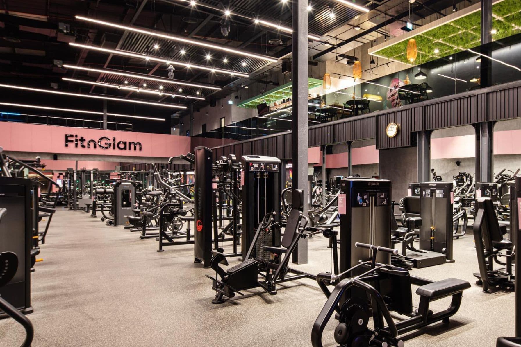 Huge training floor with wide range of gym equipment amidst brightly lit warehouse style setting with pink branding on walls.