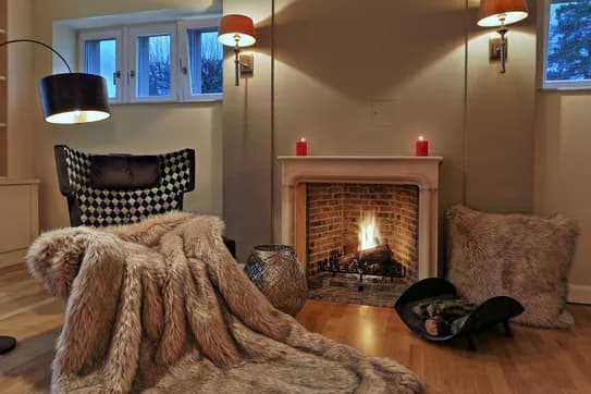 Cosy reading corner by the crackling fireplace with an armchair covered in luxurious faux fur and indirect lighting.