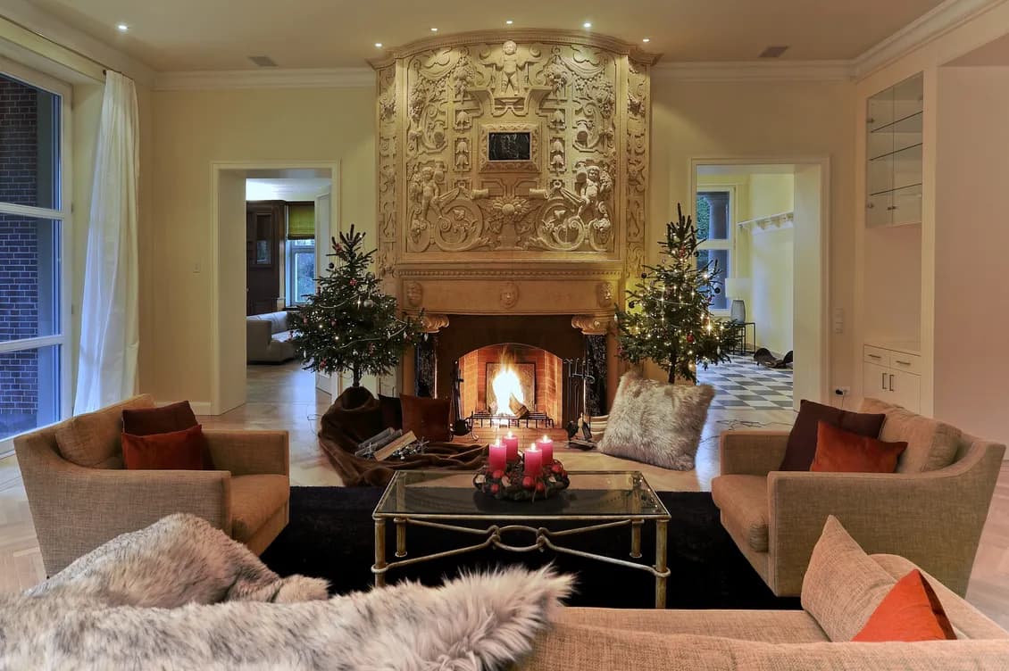 Opulent living room in classic style with large, ornate fireplace, two small Christmas trees and an elegant seating area with Advent wreath on the coffee table.