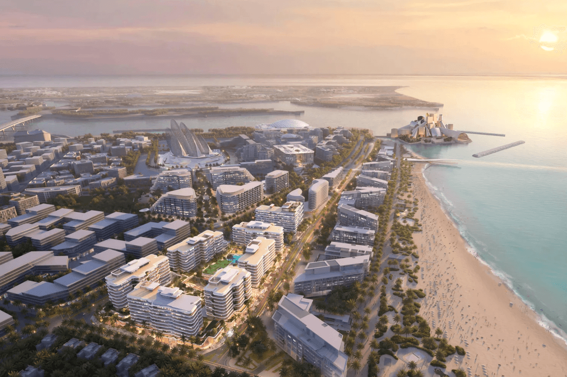 Aerial view of a coastal city at sunset, featuring modern buildings, a sandy beach, and a distant island with a structure.