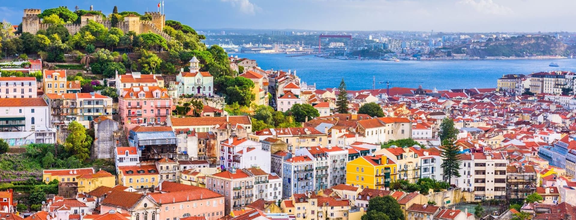 Lisbon, Portugal cityscape with colorful buildings and red tile roofs. The Tagus River and São Jorge Castle are in the background.