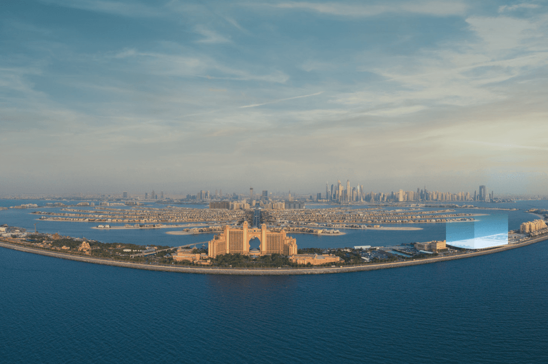 Luftaufnahme der Palm Jumeirah in Dubai, mit dem Atlantis Hotel im Vordergrund und der Skyline der Stadt im Hintergrund unter blauem Himmel.