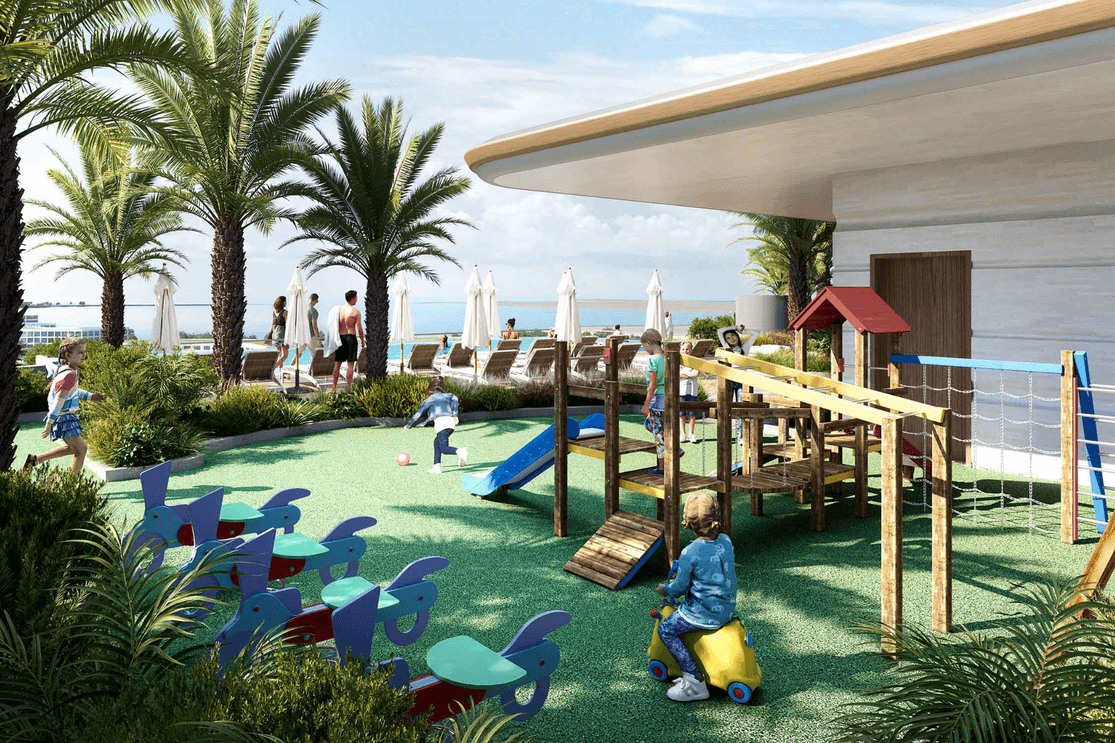 Children’s play area at Sunset Bay 5 featuring outdoor play equipment, soft flooring, landscaped greenery, and views toward the waterfront.
