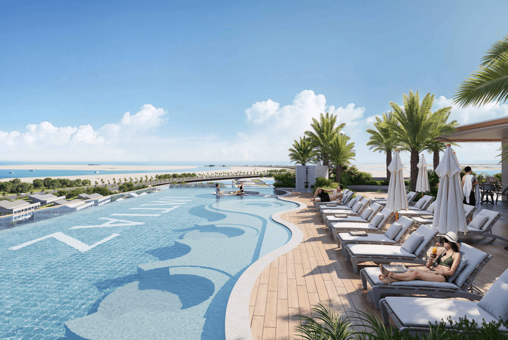 Outdoor pool area at Sunset Bay 5 featuring a large swimming pool with patterned detailing, sun loungers, shaded seating, and views across the beachfront and surrounding landscape.