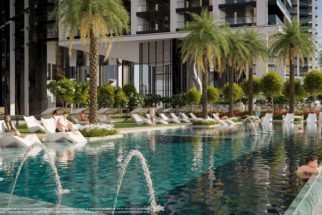 Modern outdoor pool area with palm trees, lounge chairs, and fountains. People relax by the water, surrounded by lush greenery and tall buildings.