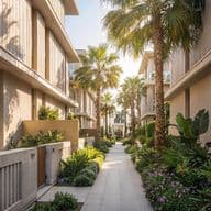 A sunny walkway lined with palm trees and lush gardens between modern residential buildings.