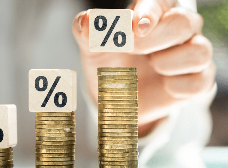 Die Hand platziert einen Prozentblock auf einem Münzstapel, der das Zinswachstum symbolisiert.