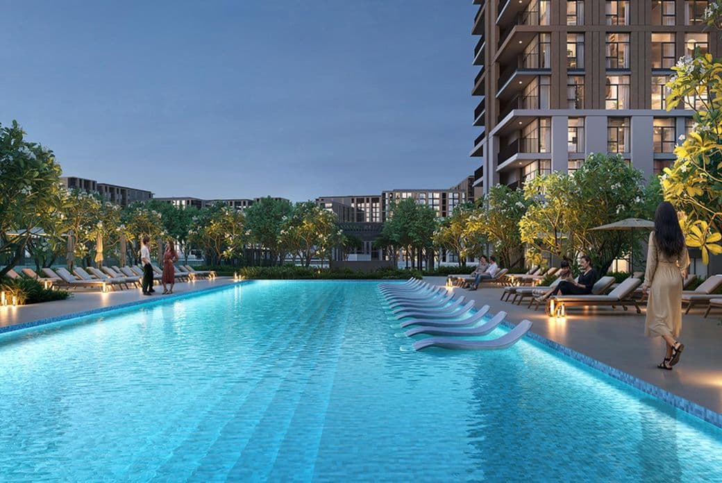 Luxurious outdoor pool at twilight with lounge chairs, leafy trees, and a modern high-rise building in the background. People are relaxing nearby.