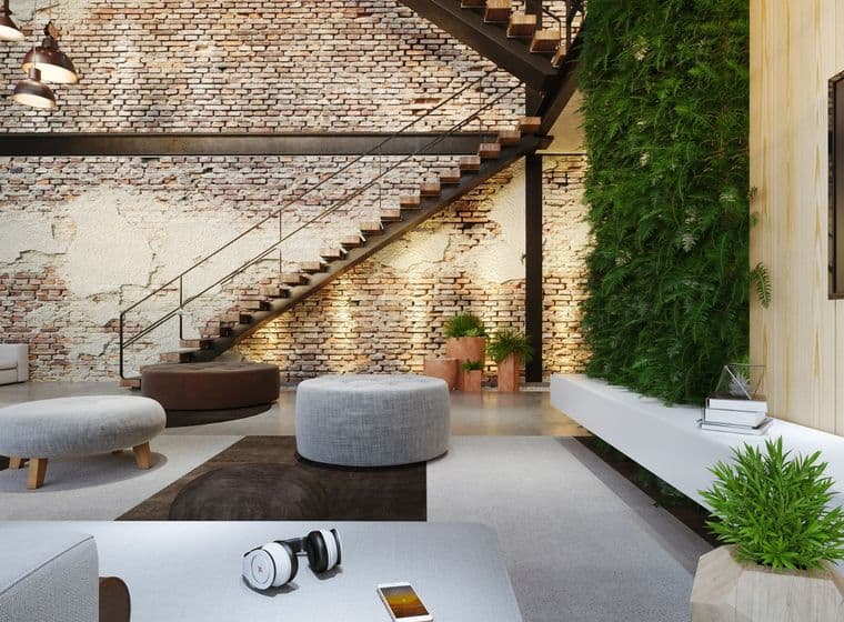 Sala d'estar amb paret de maó, escala metàl·lica i jardí vertical. S'hi veuen pufs, auriculars i un telèfon.