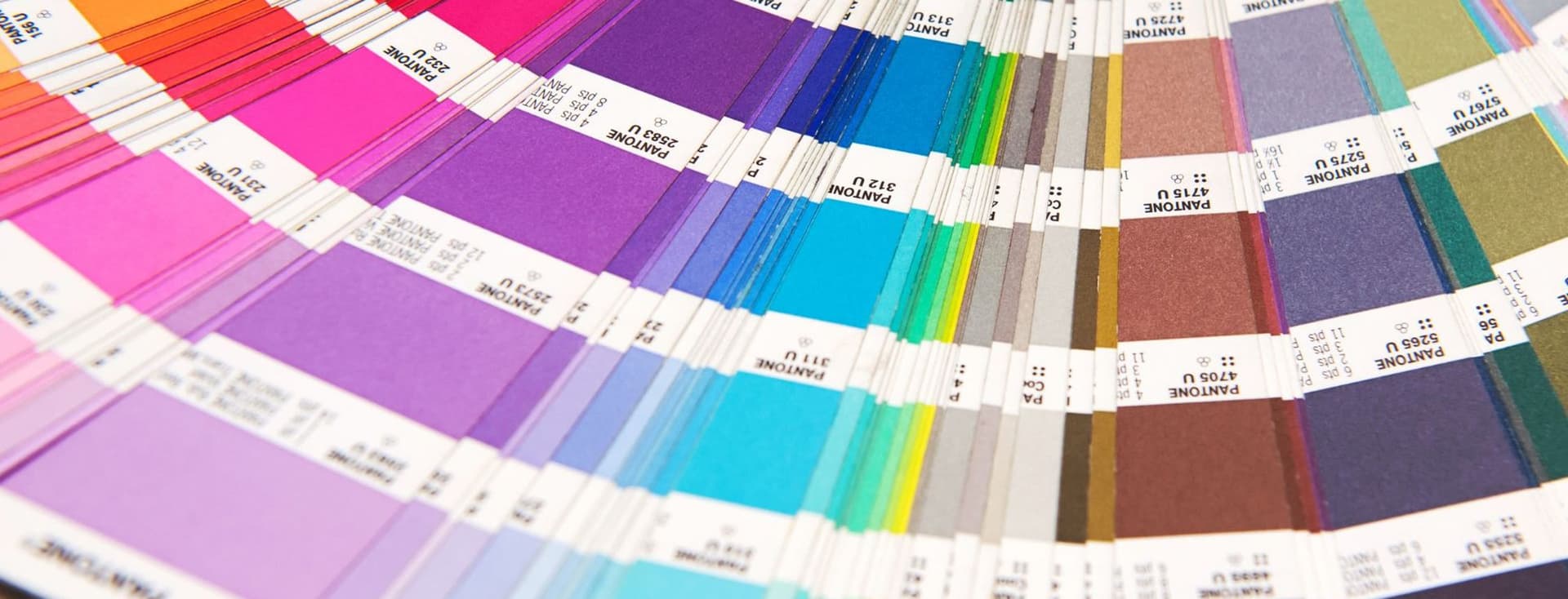 Primer pla d'un llibre de mostres de colors Pantone, obert en ventall per mostrar un espectre de tonalitats que van del vermell al morat, blau, verd i gris.