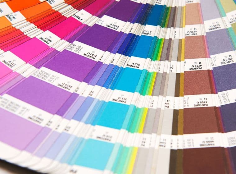 Primer pla d'un llibre de mostres de colors Pantone, obert en ventall per mostrar un espectre de tonalitats que van del vermell al morat, blau, verd i gris.