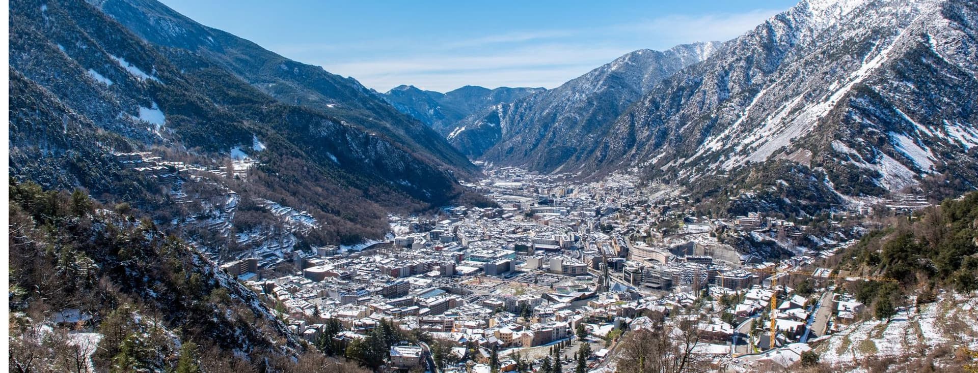Andorra la Vella cityscape nestled in a valley between snow-capped mountains under a clear blue sky.
