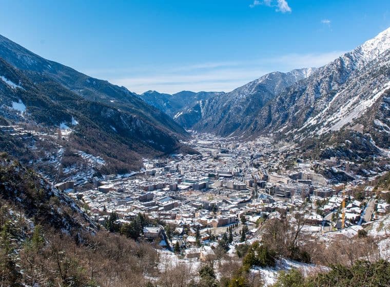 Paisatge d'Andorra la Vella enclavada en una vall entre muntanyes nevades sota un cel blau clar.
