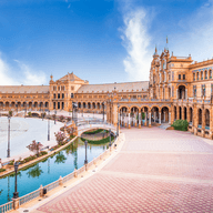 Plaza de España in Seville, Spain. Ornate orange buildings surround a canal with bridges under a blue sky.