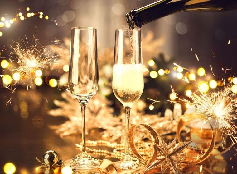 Champagner, der in ein Glas gegossen wird, mit Wunderkerzen und goldenen Dekorationen.