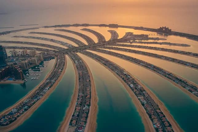 Aerial view of Palm Jumeirah at sunset, palm-shaped islands radiating from a central trunk into the sea, golden reflections on the water.