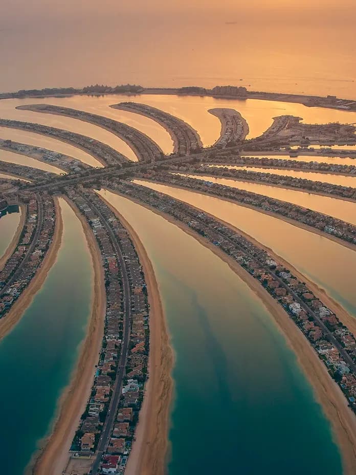 Aerial view of Palm Jumeirah at sunset, palm-shaped islands radiating from a central trunk into the sea, golden reflections on the water.