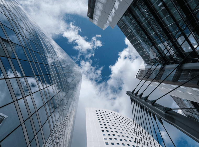 Mirant cap amunt als gratacels moderns de vidre amb un cel blau i núvols blancs.