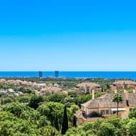 Views of Elviria from a penthouse where you can see many houses and green trees, in the background the sea and the blue sky.