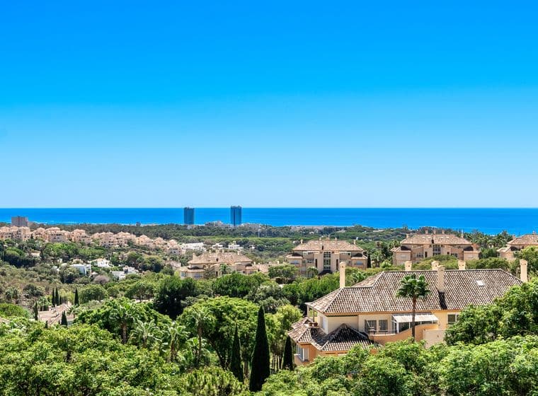 Ausblicke von Elviria aus einem Penthouse, von wo aus man viele Häuser und grüne Bäume sehen kann, im Hintergrund das Meer und den blauen Himmel.