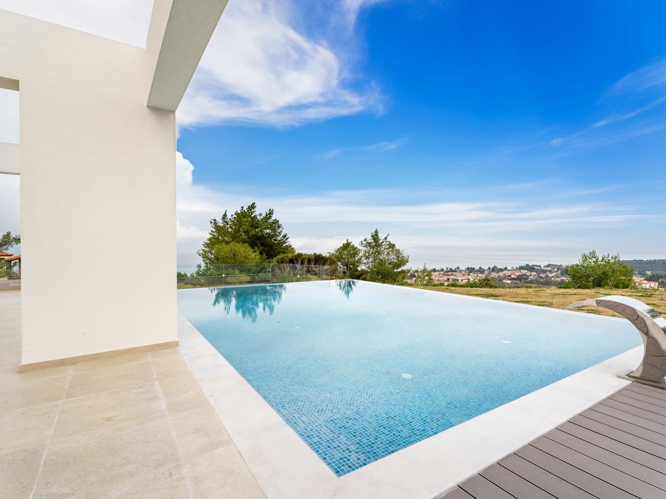 Infinity pool with blue tiles, a silver waterfall feature, and a view of the ocean and sky.