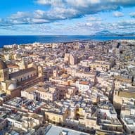 Luftaufnahme einer Küstenstadt mit einer markanten kuppelförmigen Kirche, dichter Bebauung und dem Meer im Hintergrund unter einem teilweise bewölkten Himmel.