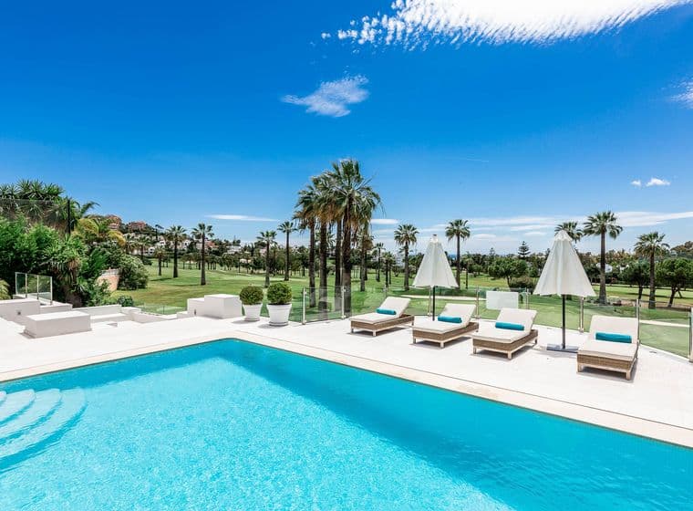 Klares Schwimmbecken neben einem grünen Golfplatz und blauem Himmel