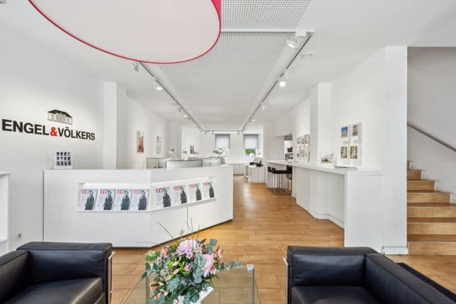 Modernes Immobilienbüro mit weißen Wänden, Holzboden, ausgestellten Broschüren und einer Treppe auf der rechten Seite.