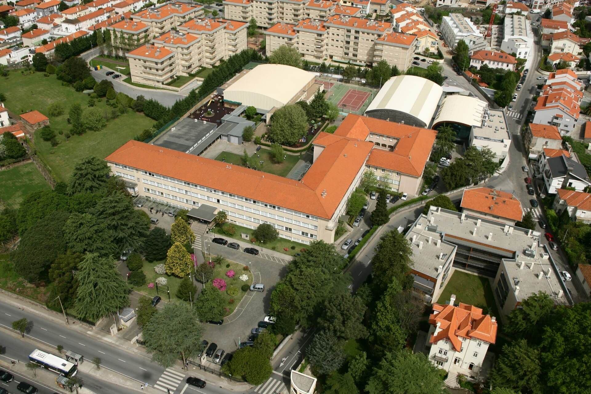 Luftaufnahme eines Komplexes mit rotbedachten Gebäuden, Grünflächen und Straßen, umgeben von Wohngebieten und Bäumen.