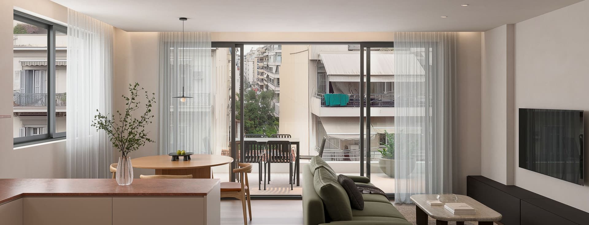 Modern living room with a green sofa, coffee table, and wall-mounted TV, leading to a balcony with outdoor seating. Natural light fills the space.