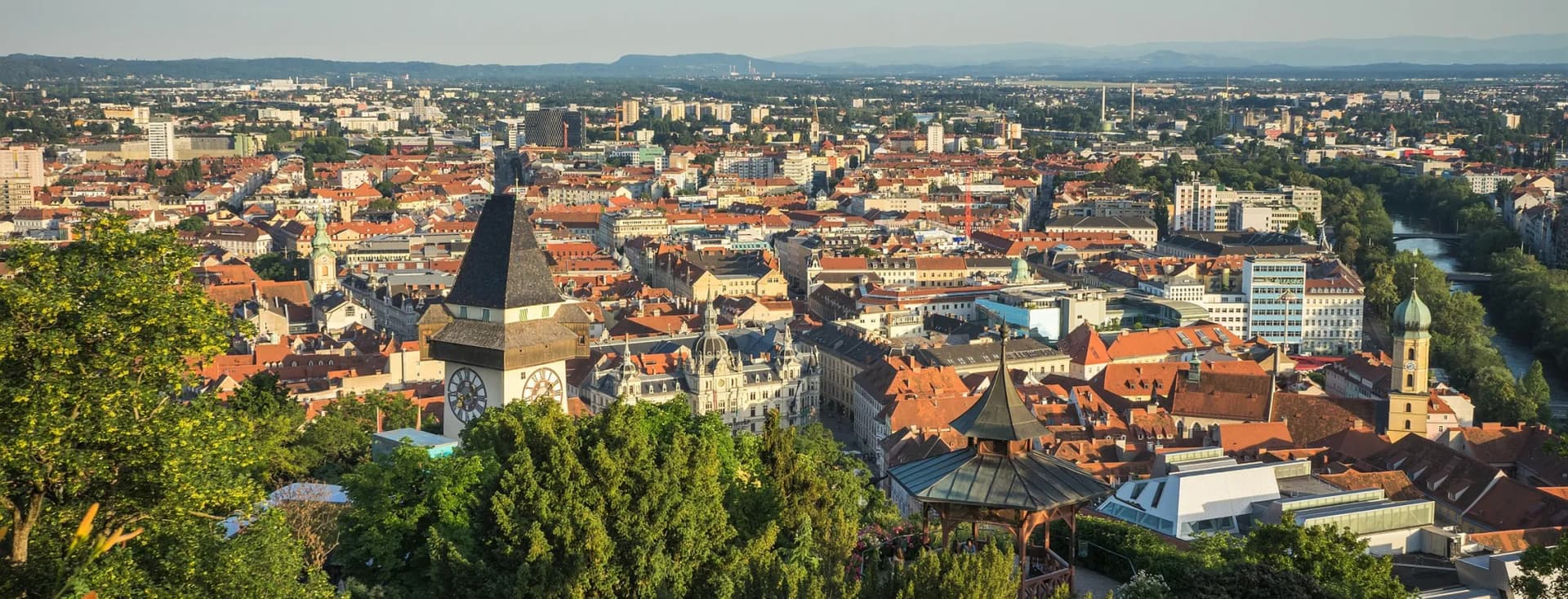 Panoramaansicht von Graz in Österreich mit roten Dächern, Kirchtürmen, einem sich schlängelnden Fluss und Hügeln in der Ferne