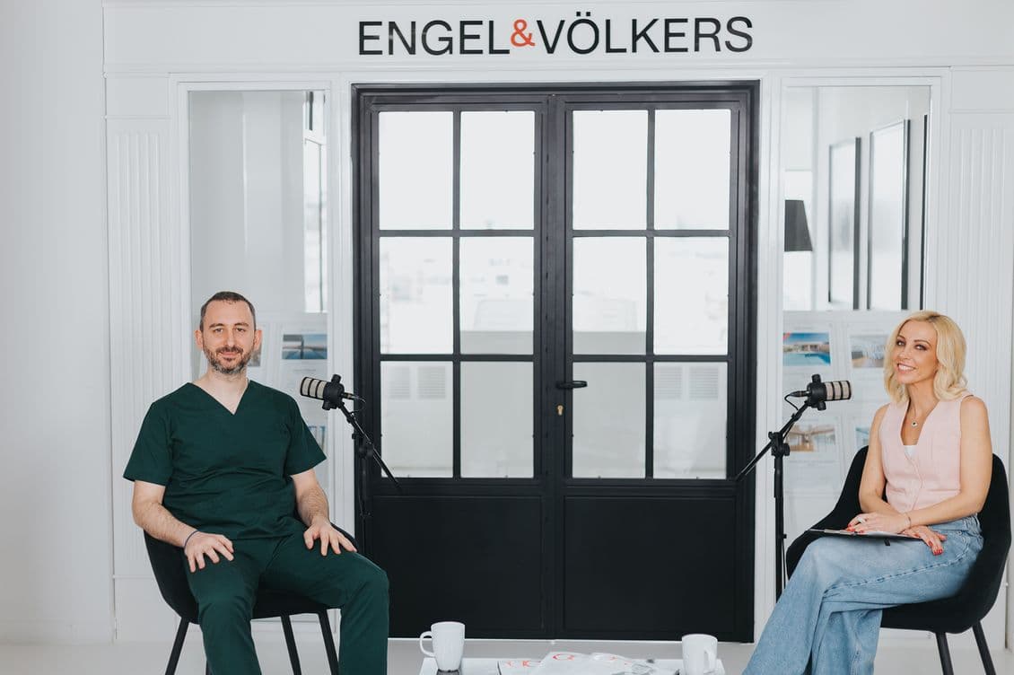 Konstantinos Peristeris and Lili Piraki seated in a bright room with microphones, under an "Engel & Völkers" sign. They appear to be engaged in a conversation.