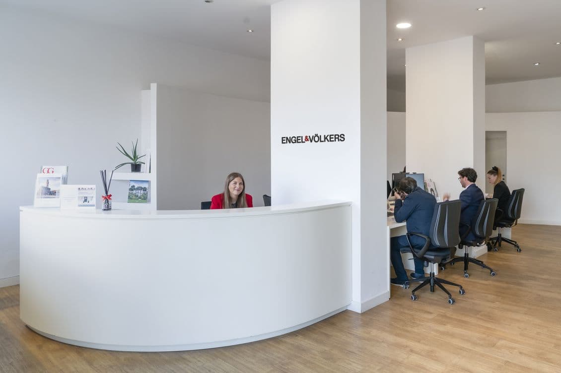 Modern office with a curved white reception desk, a smiling receptionist, and employees working at desks in the background.