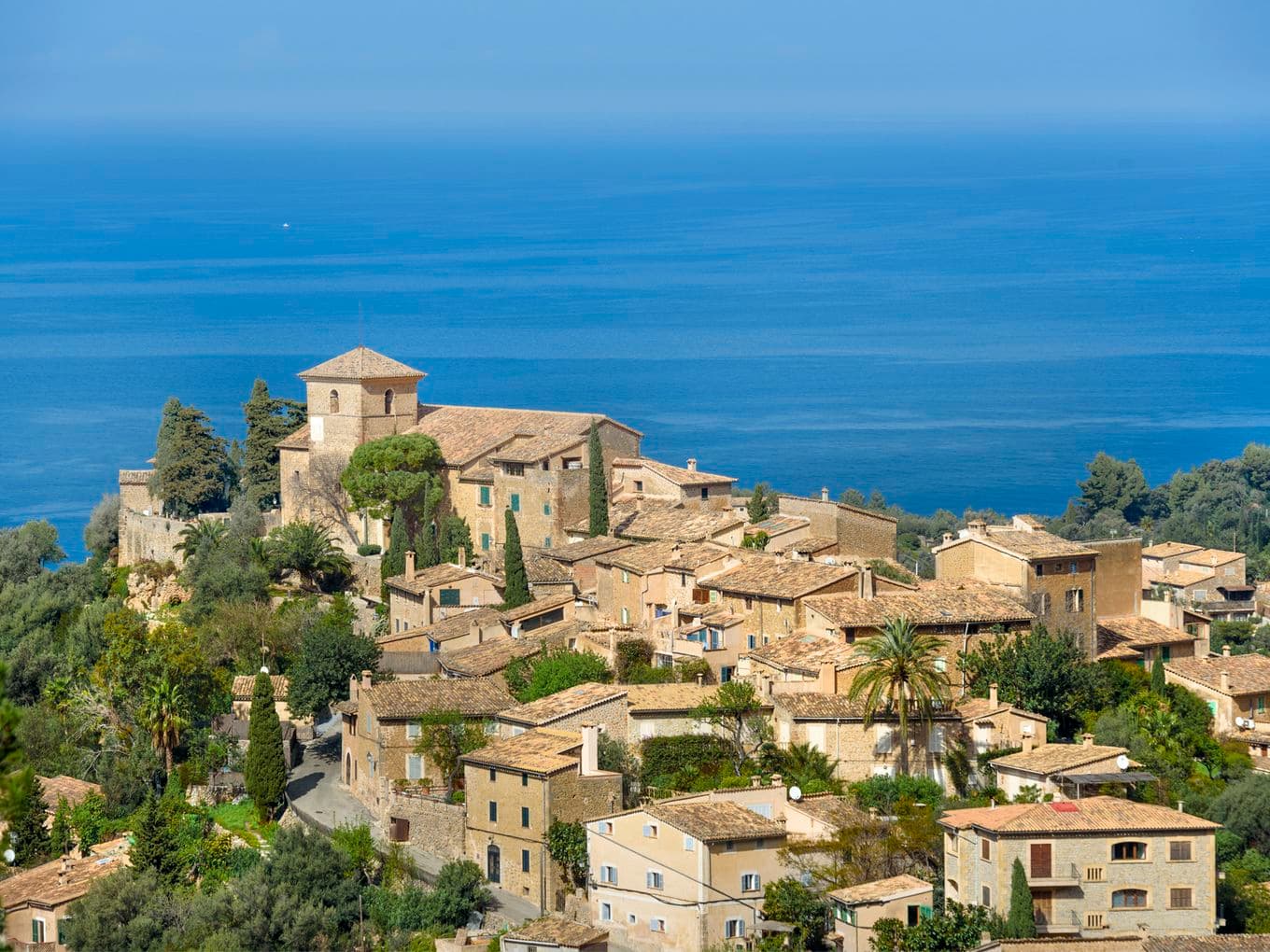 Panoramic aerial view of Deià village nestled in the Tramuntana mountains with the Mediterranean Sea in the background