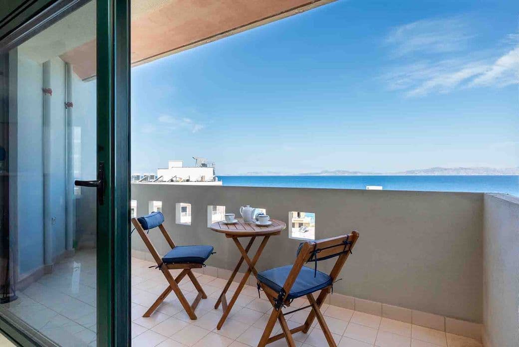 Balcony with two chairs and a small table set for tea, overlooking a serene ocean view under a clear blue sky.