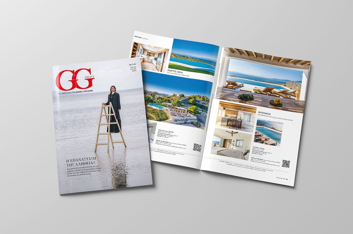 A Greek magazine with an outdoor cover is open to pages showcasing luxurious resorts with coastal views and elegant interiors.