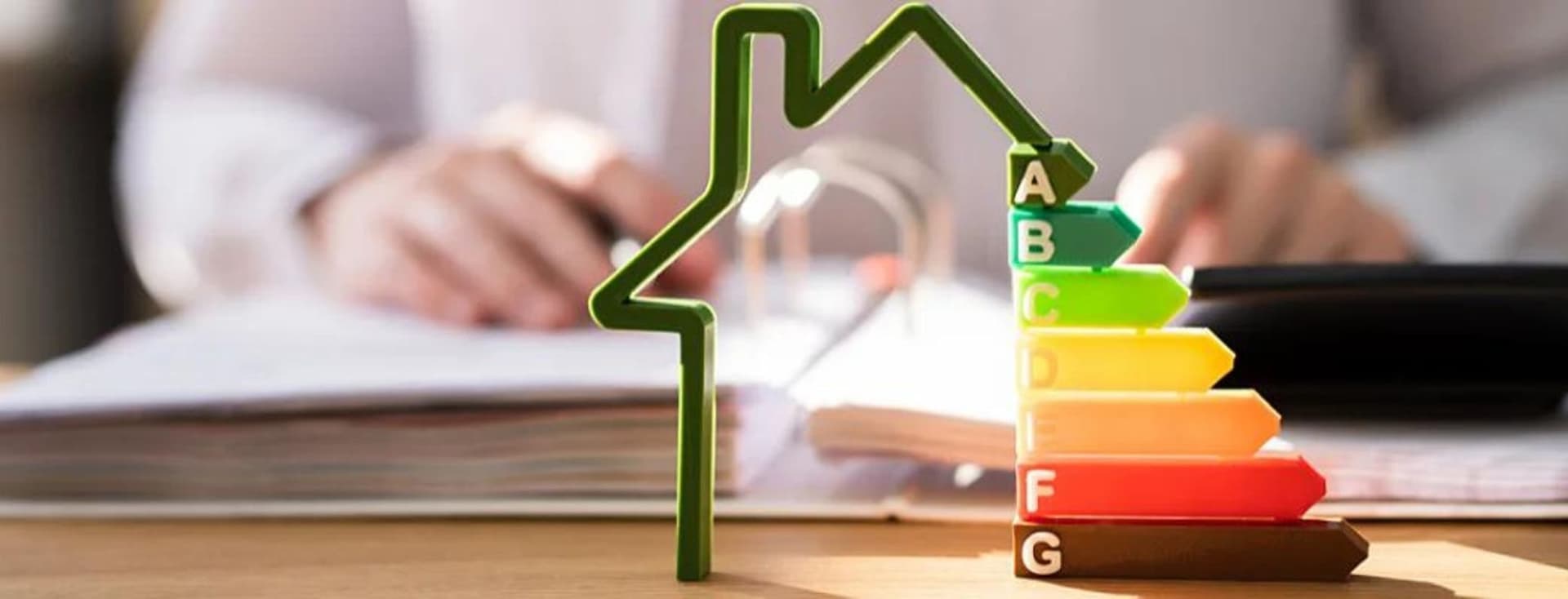 Haus mit Energieeffizienzklassen von A bis G, Person arbeitet am Schreibtisch, Symbol für nachhaltige Immobilien