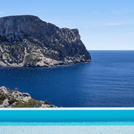 Infinity pool overlooking the blue sea with a rocky cliffs and palm trees.