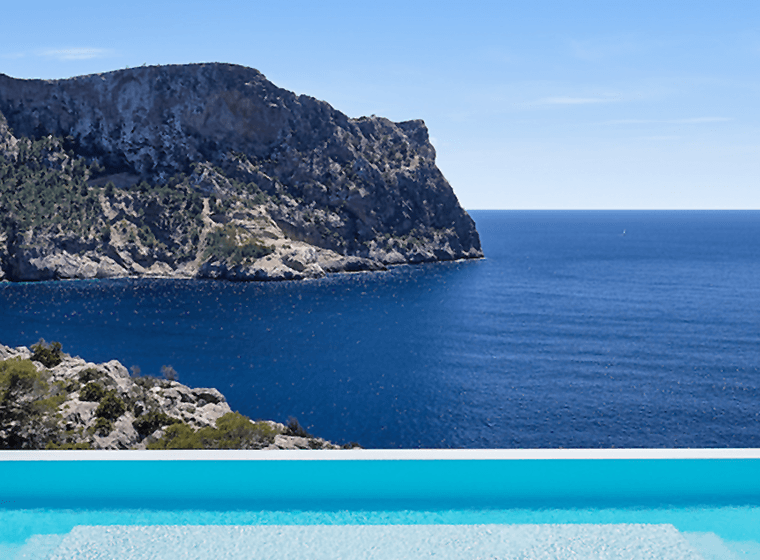 Infinity pool overlooking the blue sea with a rocky cliffs and palm trees.
