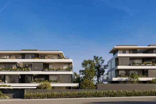 Two modern three-story apartment buildings with layered white balconies, planted terraces and trees under a clear blue sky.